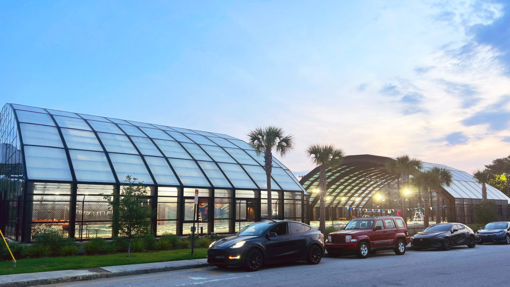 DynaDome | Two cars parked in front of a glass building at dusk with a retractable enclosure.