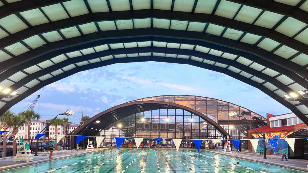 DynaDome | A retractable enclosure allows for a swimming pool to be used under a building at dusk.