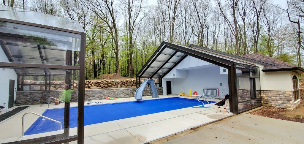 DynaDome | A swimming pool with a retractable enclosure in a backyard.