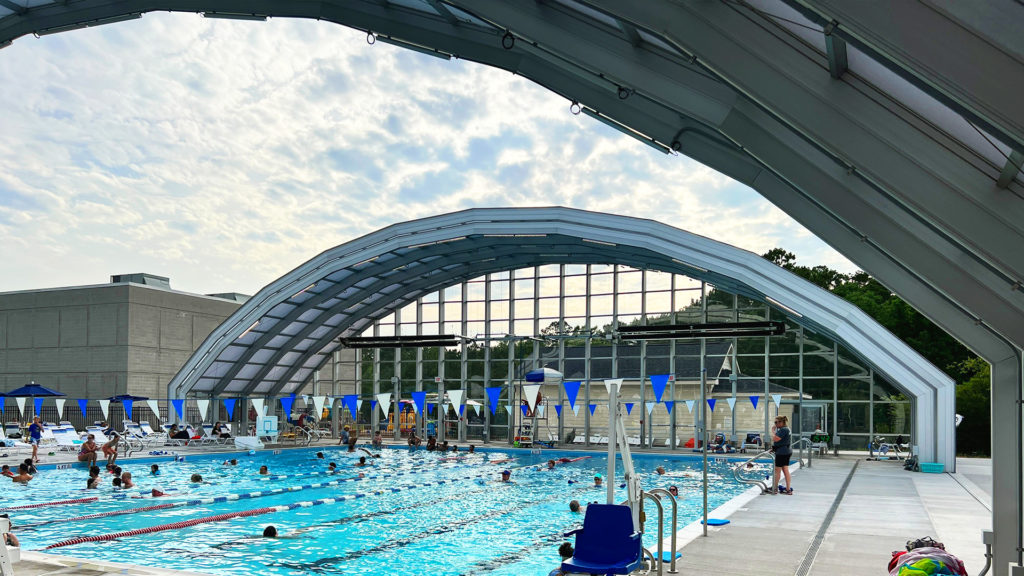 DynaDome | A retractable enclosure over a swimming pool with people in it.